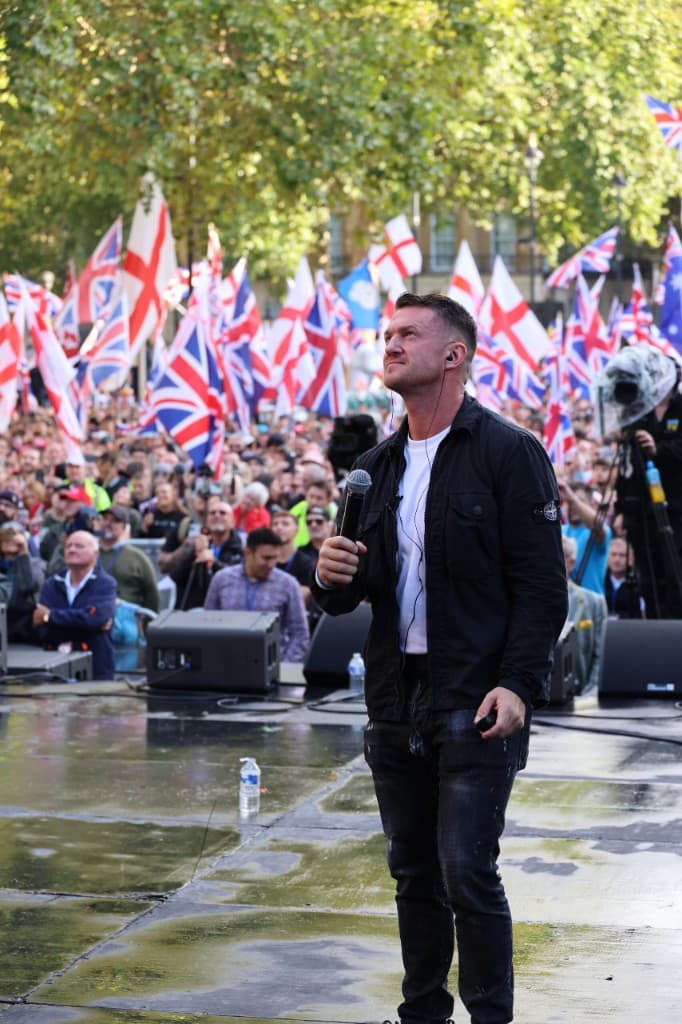 Speaker on stage at a UTK event with crowd and UK flags